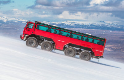 Sleipnir Truck fährt einen steilen Gletscher hoch für die Eishöhlen und Gletscher Expedition. Schneebedeckte Berge sind in Hintergrund zu sehen