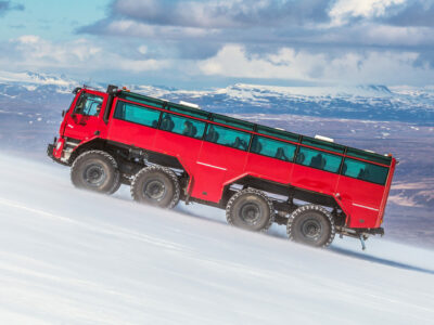 Sleipnir Truck fährt einen steilen Gletscher hoch für die Eishöhlen und Gletscher Expedition. Schneebedeckte Berge sind in Hintergrund zu sehen